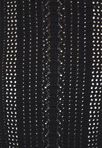 Tessuto all'uncinetto nero con un motivo di punti alternati pieni e aperti, con linee verticali testurizzate e un elemento di design distintivo.