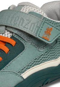 Sportieve schoen in teal en grijs met een bovenwerk van mesh, oranje veters, klittenbandsluiting en een rubberen zool met een konijnlogo.