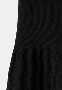 Schwarzer Strickstoff mit gerippter Struktur und gerafftem oder gerüschtem Detail nahe dem unteren Rand.