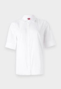 Chemise blanche à manches courtes avec boutons, col et logo discret sur la poitrine, présentée sur un fond clair uni.