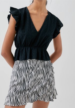 Femme portant un haut noir texturé sans manches avec des manches à volants et une jupe imprimée zébrée noir et blanc avec un ourlet à volants.