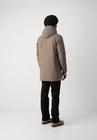 Chaqueta aislante color marrón claro con capucha, mangas largas y corte recto, combinada con pantalones negros y zapatos color beige. Diseño simple, sin estampados.