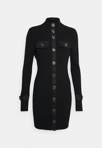 Svart stickad klänning med hög krage, med en framknäppning med guldhuvuden, två bröstfickor med lock och manschetter.