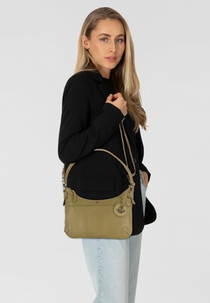 Sac bandoulière en cuir vert avec un design courbé, des finitions en argent et un détail d'accent rond. Porté par une personne avec de longs cheveux.