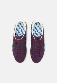Violet nubuk urheilukengät, joissa on vihreitä yksityiskohtia ja teksturoitu pohja. Varusteena nauhakiinnitys ja Reebok-merkitty sisäpohja.