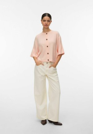 Lühikeste varrukatega roosa kootud kardigan pruunide nööpidega, millele on lisatud laiad valged püksid ja tumedad kontsakingad. Tekstureeritud kangas on nähtav.