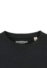 Camiseta de algodón negra con cuello redondo y mangas cortas; presenta un logo en blanco de "Pink Floyd" en la etiqueta del cuello. Textura lisa.