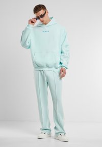 Una sudadera verde menta con un bolsillo delantero y un diseño de paisley en la manga, combinada con pantalones a juego y zapatillas blancas.