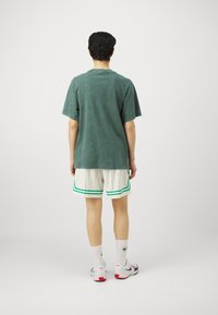 Groene T-shirt met korte mouwen en een relaxed fit, gecombineerd met witte shorts met een streepjesmotief en groene accenten, witte crew-sokken en sportieve schoenen.