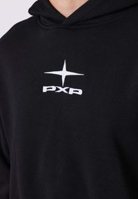 Zwarte hoodie met een zachte textuur, voorzien van een witte geborduurde logo "PXP" en een sterontwerp. De capuchon is duidelijk zichtbaar.