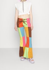 Pantalons évasés en patchwork de coton multicolore dans des teintes vives de rose, jaune, orange, bleu et marron, avec un détail de laçage à l'avant.