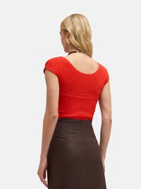 Haut rouge à côtes avec un dos plongeant, manches courtes, et un design ajusté, associé à une jupe marron foncé avec une fermeture éclair au dos.