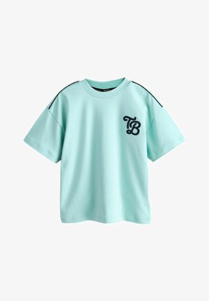 Jasnoniebieska bawełniana koszulka z krótkim rękawem, z czarnym haftowanym logo "TB" na przodzie oraz czarnymi akcentami szwów na ramionach.