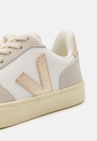 Sneaker con una toma in pelle bianca liscia, dettagli in suede grigio chiaro e un logo beige testurizzato sul lato. Suola in gomma color crema.