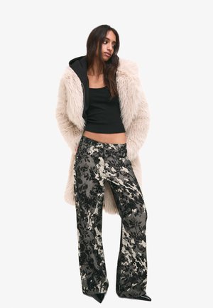 Faux fur ljusbeige kappa, svart croptopp, mönstrade svarta och grå vida byxor, spetsiga svarta skor, släta texturer och distinkt blommönster.