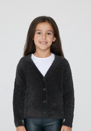 Donkergrijze, fluffy cardigan met een v-hals, lange mouwen en vijf zwarte knopen aan de voorkant, gecombineerd met een wit shirt en zwarte broek.