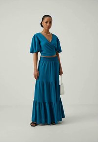 Teal tweed set met een wikkeltop met korte pofmouwen en een gelaagde maxi-rok, gemaakt van gestructureerde stof met een gerimpelde taille.