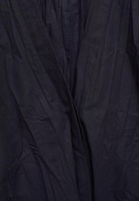 Tamno plava tkanina glatke teksture, s patentnim zatvaračem na sredini i suptilnim detaljima šivanja. Ovdje ima naglašenu teksturu. 