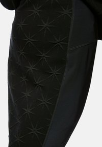 Schwarze Sportleggings mit strukturiertem Sternmuster auf einer Seite und glattem Stoff auf der anderen. Verfügt über Nähte entlang der Säume.