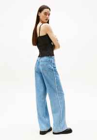Jeans anchos de tiro alto en azul con una costura lateral deshilachada, combinados con una blusa negra ajustada de tirantes finos.