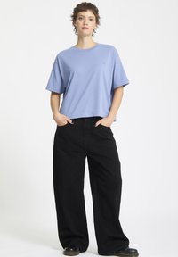 T-shirt azzurro chiaro a maniche corte, con taglio rilassato e colletto rotondo. Abbinato a pantaloni neri larghi e calzature nere. Design semplice, senza fronzoli.