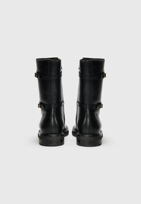 Botas de cuero negras hasta el tobillo con dos correas con hebillas, punteras redondeadas y tacones bajos apilados. Textura suave y diseño sencillo.