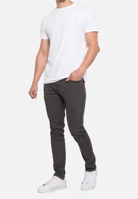 Valkoinen lyhythihainen t-paita, yhdistetty tummanharmaisiin slim-fit-farkkuihin ja valkoisiin lenkkareihin. Yksinkertainen muotoilu, sileä kankaan pinta, vähäiset yksityiskohdat.