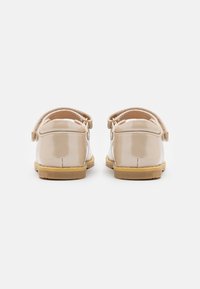 Beige patenttanska kengät, joissa on sileä pinta, takanauhalla ja kumipohjalla, näkymä takaapäin.