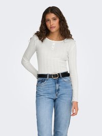 Biele rebrované tričko s dlhým rukávom, okrúhlym výstrihom a zapínaním na tri gombíky. Kombinované s modrými džínsami s vysokým pásom a čiernym opaskom.
