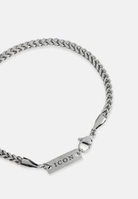 Bransoletka z metalowego łańcuszka o polerowanym srebrnym wykończeniu, z plecionymi ogniwami oraz prostokątną zawieszką z grawerunkiem "ICON". Zapięcie typu lobster.