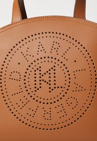 Borsa a spalla in pelle tan con design del logo perforato e motivo circolare, manici piatti e texture liscia. Ideale per l'uso quotidiano.
