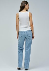 Top de tirantes blanco de canalé combinado con jeans rectos de mezclilla azul claro, con bolsillos traseros y un corte holgado. Unos zapatos negros de tacón alto completan el conjunto.