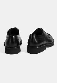 Schwarze Lederschuhe mit glatter Oberfläche, abgerundeter Zehenpartie und einer dicken schwarzen Gummisohle. Sie verfügen über minimale Nähte und ein klassisches Design.