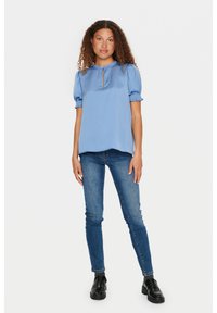Blusa di raso azzurro chiaro con maniche corte a sbuffo, dettaglio del colletto a chiave, abbinata a jeans skinny blu scuro e stivaletti neri slip-on.