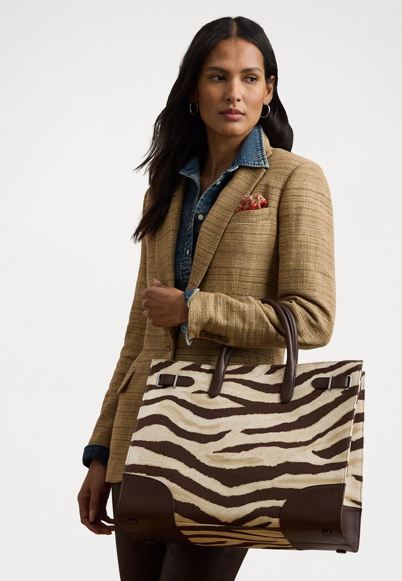 Zebra-print draagtas van stof met bruin leren accenten. Beschikt over dubbele bovenhandvatten en metalen beslag voor sluiting.