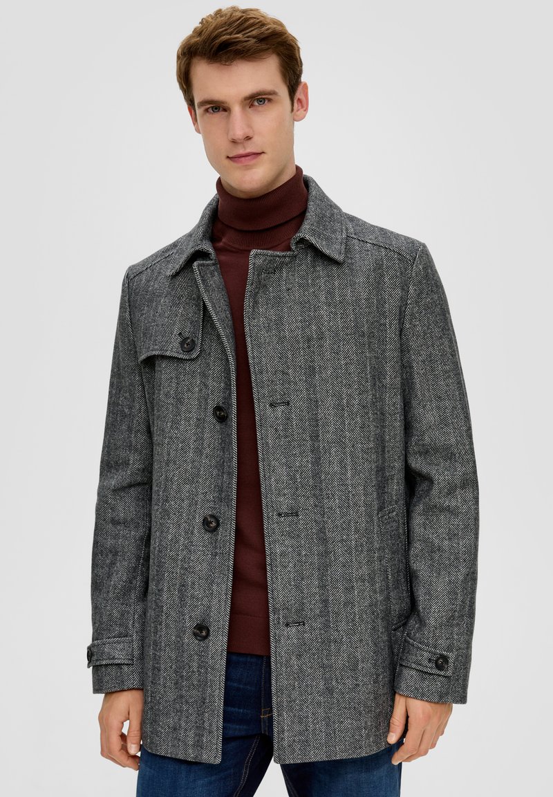 Grau-karierter Mantel mit Kragen, Knopfverschluss und seitlichen Taschen. Getragen über einem weinroten Rollkragenpullover und blauen Jeans, im lässigen Schnitt.