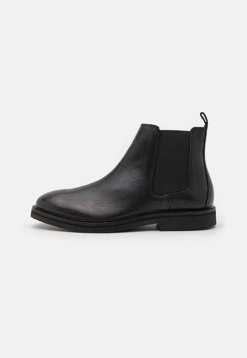 Botín Chelsea negro de cuero con paneles elásticos en los laterales, puntera redonda y suela de goma texturizada. Cuenta con una lengüeta para ponérselo fácilmente.