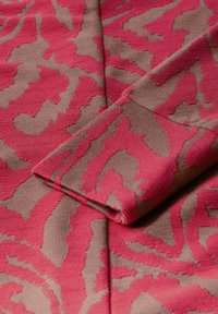 Tissu présentant un motif texturé en rose et taupe, avec des formes organiques ondulées. Le matériau semble doux, avec une légère texture rainurée.