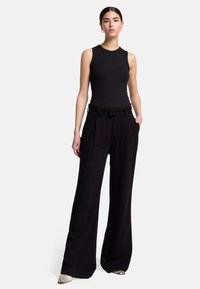 Débardeur noir à côtes associé à un pantalon noir à taille haute et jambes larges. Le pantalon présente des plis et des poches latérales ; les chaussures sont ornées d'une impression serpent.