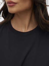 Közelkép egy nő alsó arcáról és nyakáról, hosszú barna hajjal, egyszerű fekete nyakú pólóban.