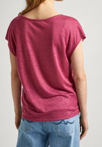 Maglietta a maniche corte, dal taglio morbido in tessuto magenta melangiato, con scollatura ampia e texture soffice, abbinata a jeans blu chiaro.