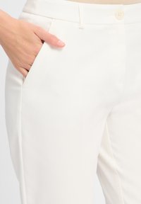 Weiße maßgeschneiderte Hosen aus subtil strukturiertem Stoff, mit Seitentaschen und einem einzelnen Knopfverschluss an der Taille.