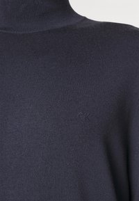 Granatowy sweter z golfem w prążki z subtelnym logo "CK" na piersi, charakteryzujący się miękką fakturą i dopasowanym krojem.