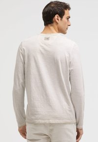 Helles graues Langarm-T-Shirt mit strukturiertem Finish, Rundhalsausschnitt und kleinem Etikett am hinteren Kragen. Glattes Material, normale Passform.