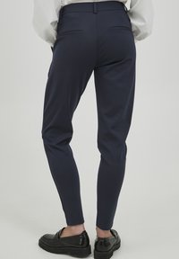 Námořnické slim-fit kalhoty s hladkým povrchem, se dvěma zadními kapsami a středním pasem. Noseny s černými platformovými botami.