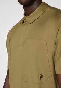 Oliwkowa koszulka polo z wyraźnym kołnierzykiem, plisą na guziki oraz naszywaną kieszonką z kontrastowym emblematem na dolnej stronie.