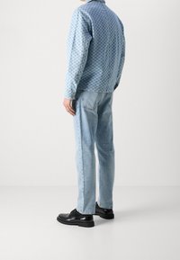 Denim jacket in blue checkered pattern, paired with light blue jeans and black leather shoes. Features a classic collar and buttoned cuffs.