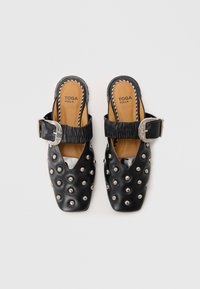 Black leather mules with a pointed toe, silver studs, and a textured strap featuring a large buckle; lined in tan leather.