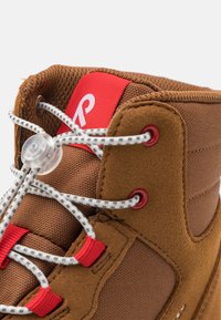 Las zapatillas altas marrones presentan una combinación de tejido texturizado y gamuza, ojetes rojos y cordones blancos con un patrón y un cierre de tipo toggle.