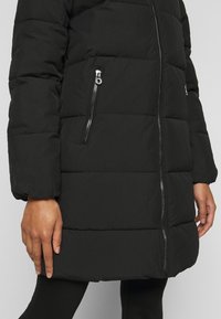 Sort puffer-jakke med et quiltet design, med sidelommer, rett snitt og elastiske mansjetter for ekstra varme.